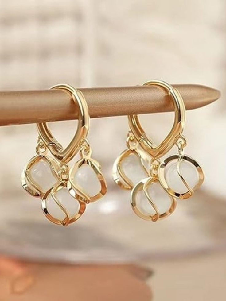 Gold hoop earrings with interlocking designs on a wooden stick against a blurred background