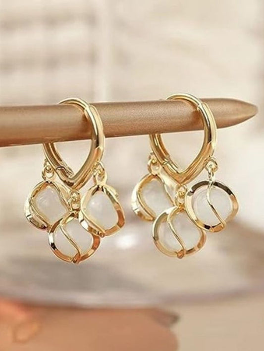Gold hoop earrings with interlocking designs on a wooden stick against a blurred background